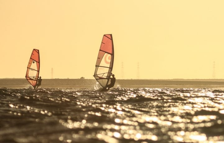 Three windsurfers sailing across Dakhla Lagoon against a golden sky